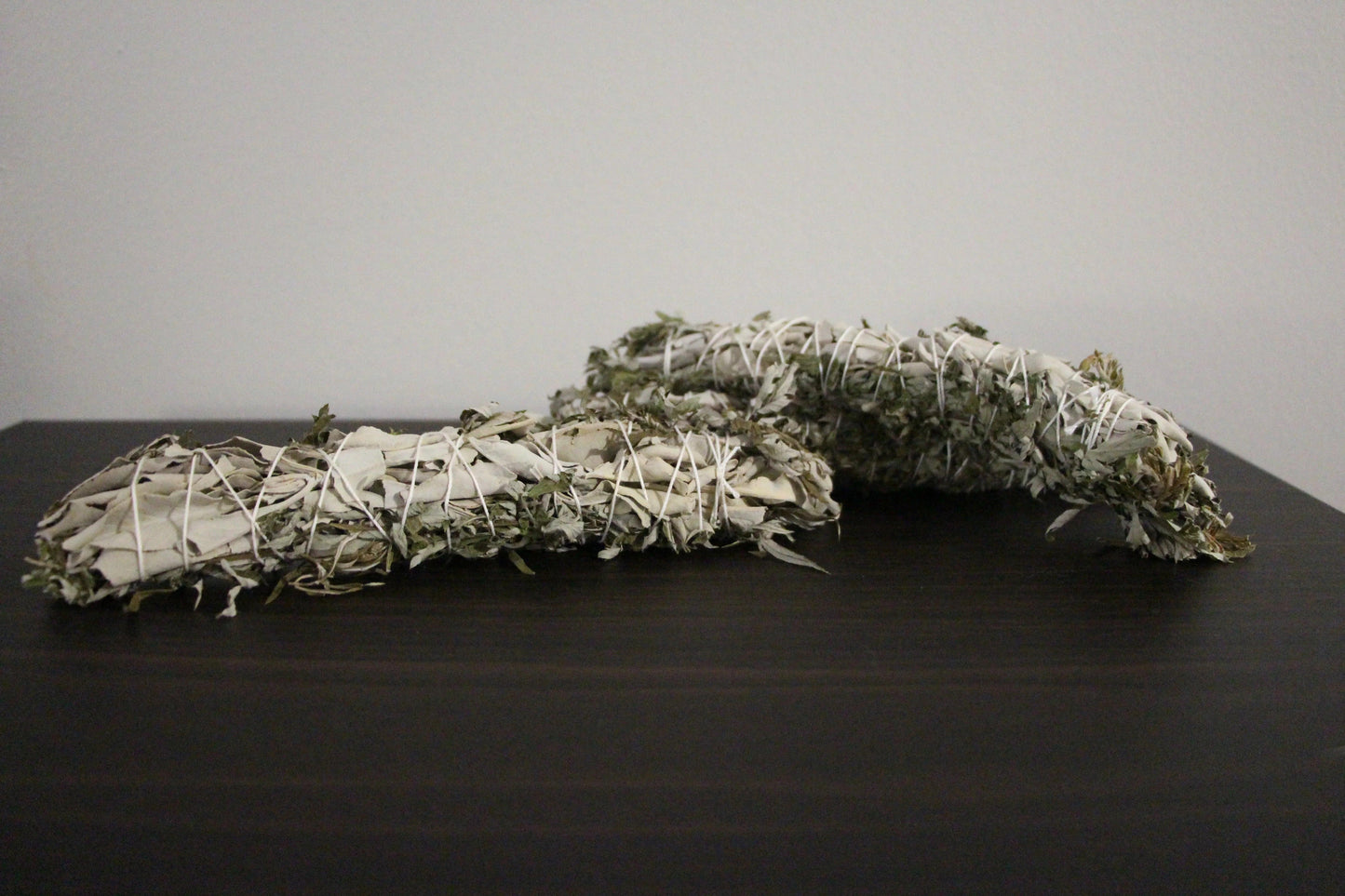 Hand-crafted sage bundles wrapped in white string on a dark wooden surface