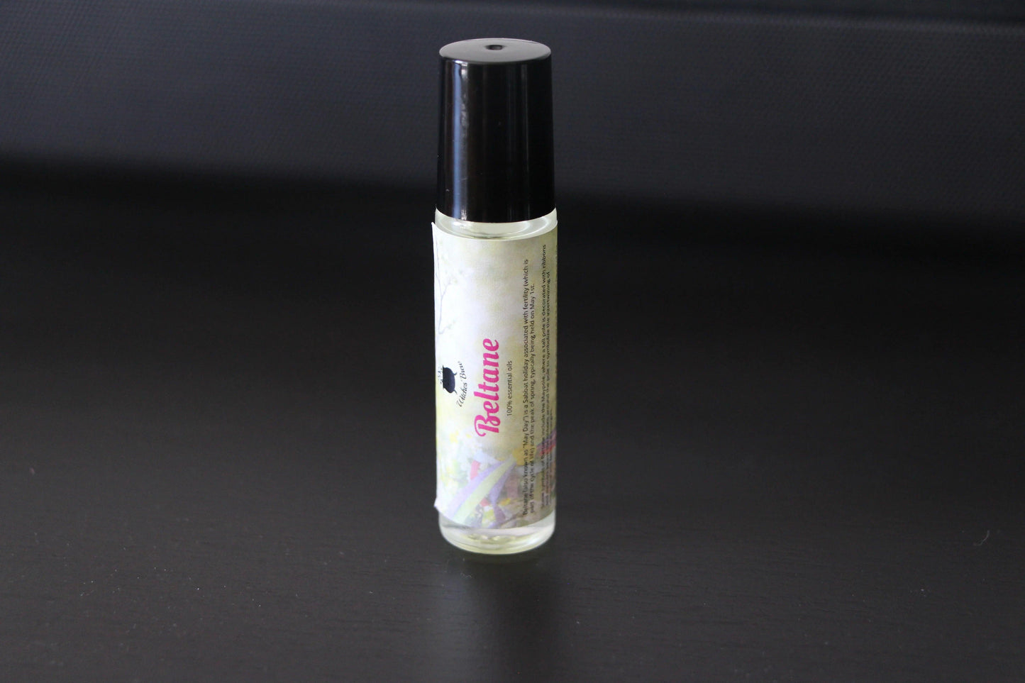 Beltane essential oil roller bottle with black cap on a dark surface, ritual aromatherapy