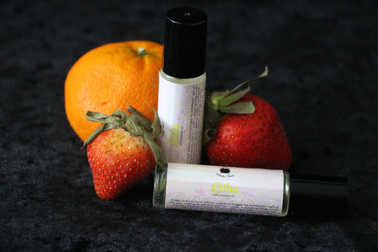 Witches' Brew Litha essential oil roller bottles with strawberries and an orange on black fabric