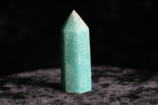 Polished green amazonite crystal standing upright on dark textured surface with black background