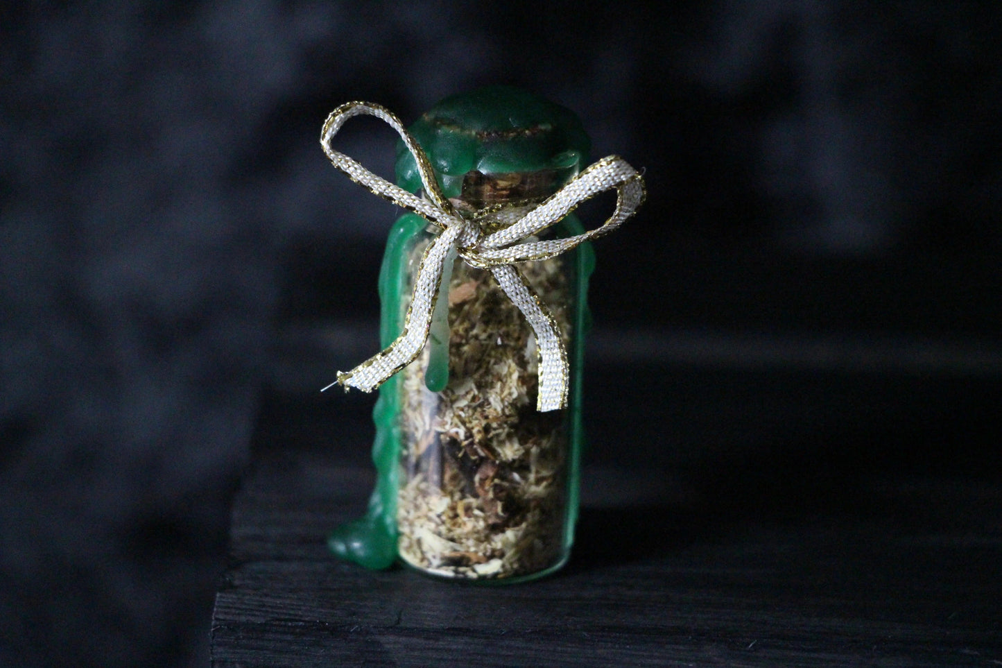 Herbal spell jar with green wax and gold ribbon, witchcraft ritual tool on dark background