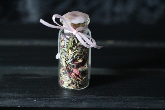 Small glass bottle with dried herbs and pink ribbon, witchcraft ritual decor