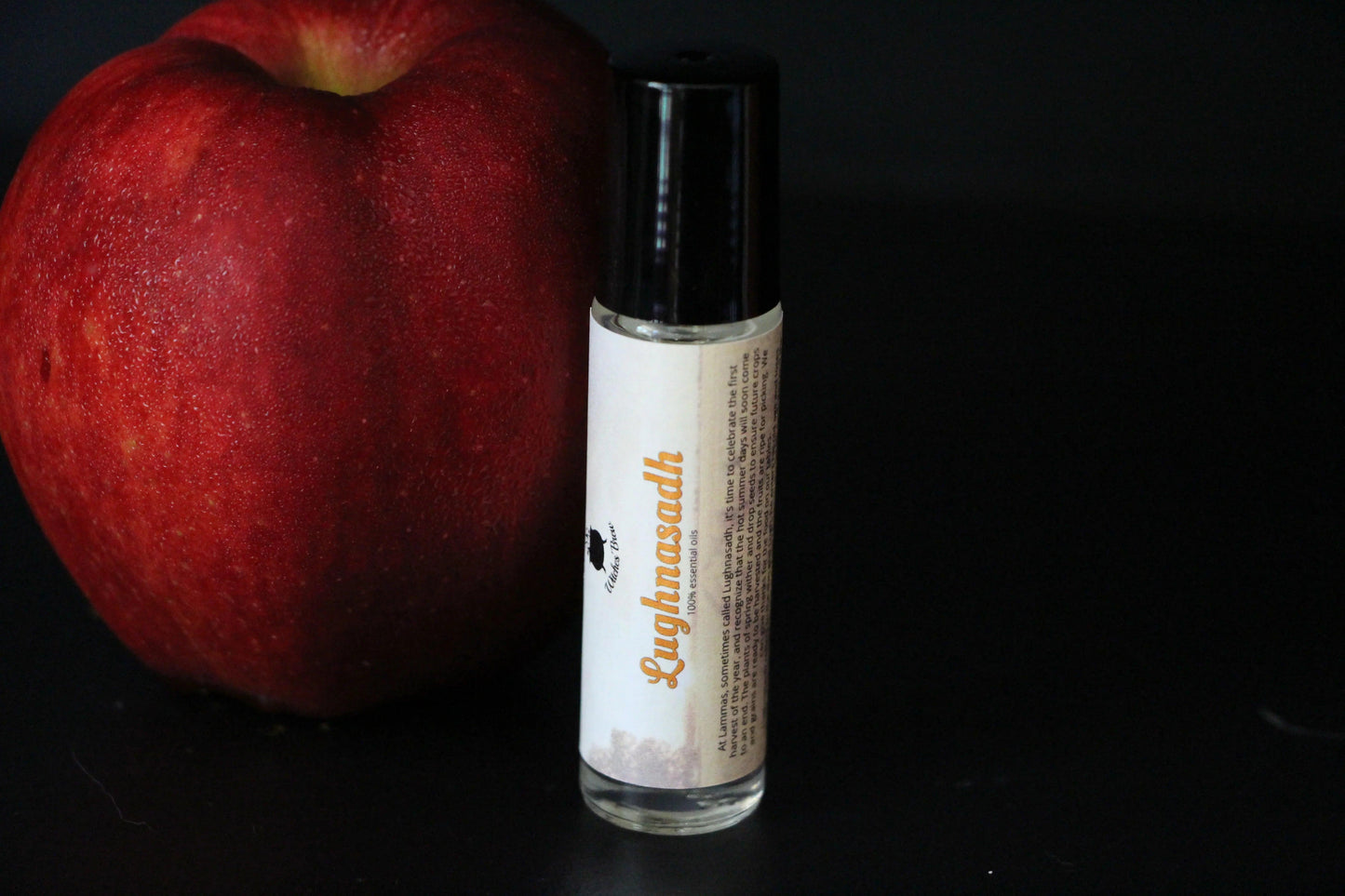 Lughnasadh essential oil roll-on and red apple on black background, sustainable witchcraft goods