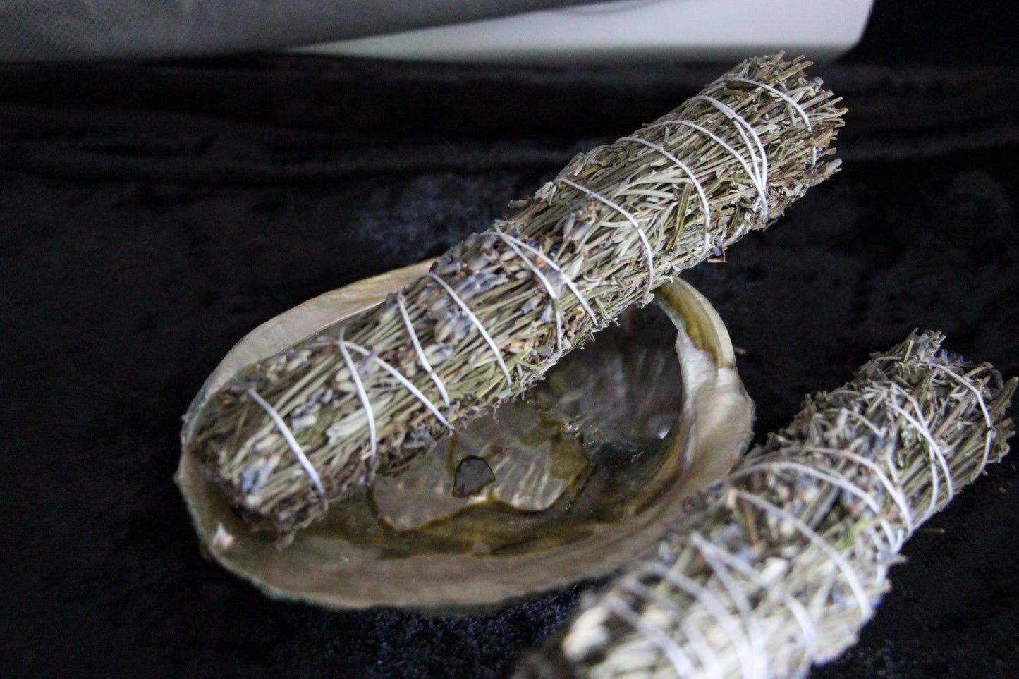 Handcrafted sage bundles with lavender in abalone shell on black velvet for ritual cleansing
