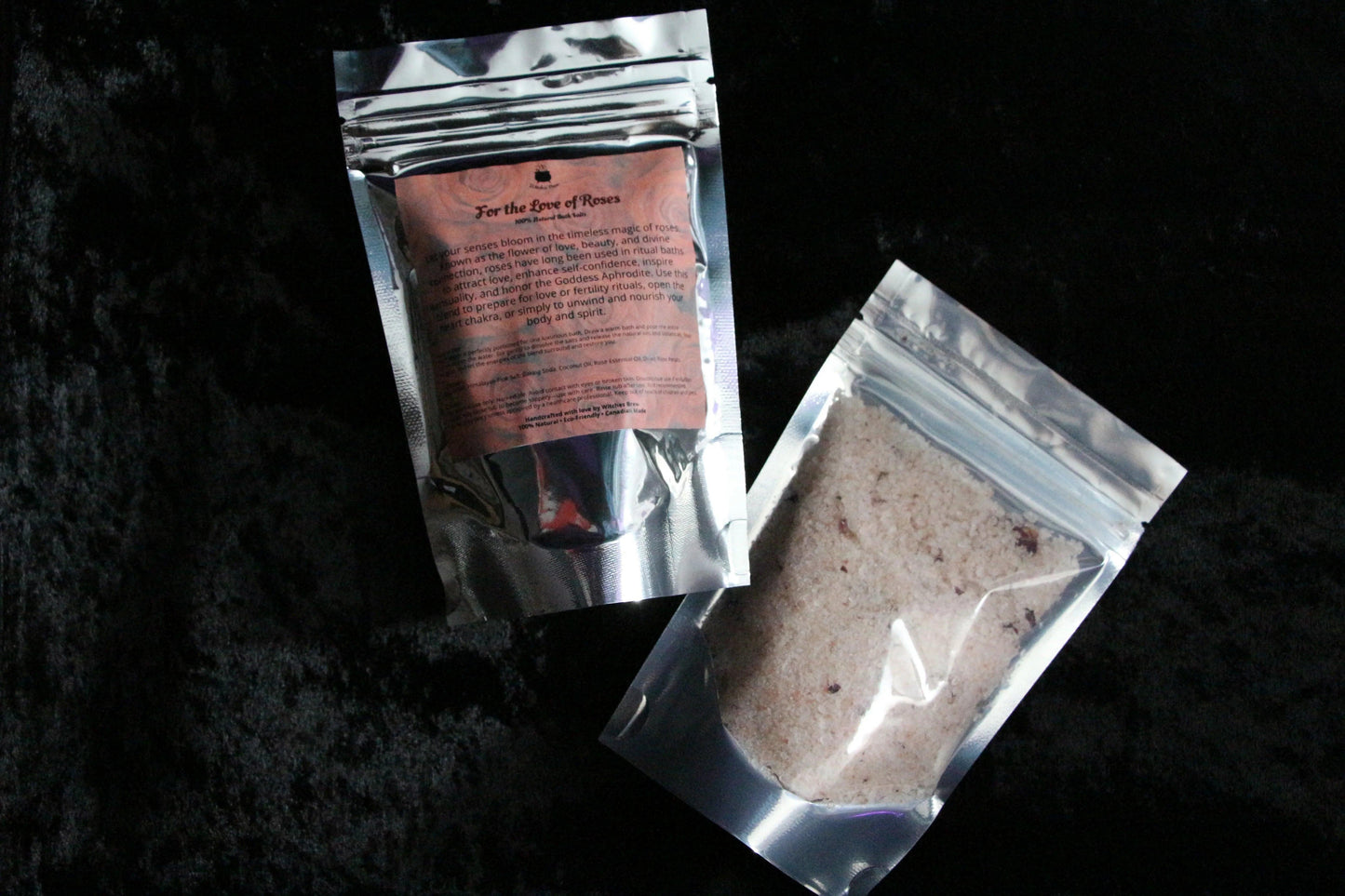 Two silver resealable bags of rose-scented bath salts on black fabric background