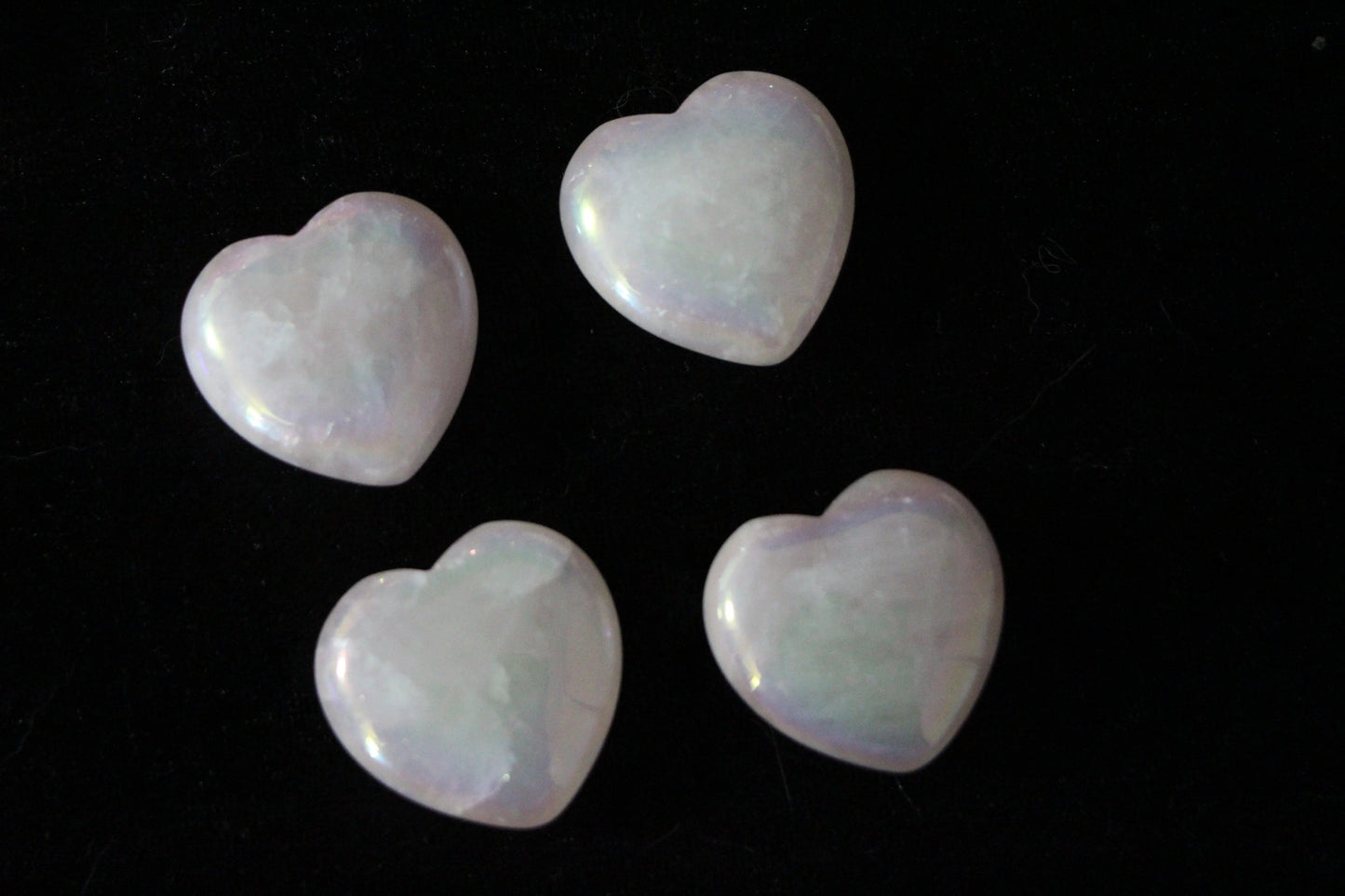 Four polished pink aura rose quartz heart crystals on a black background