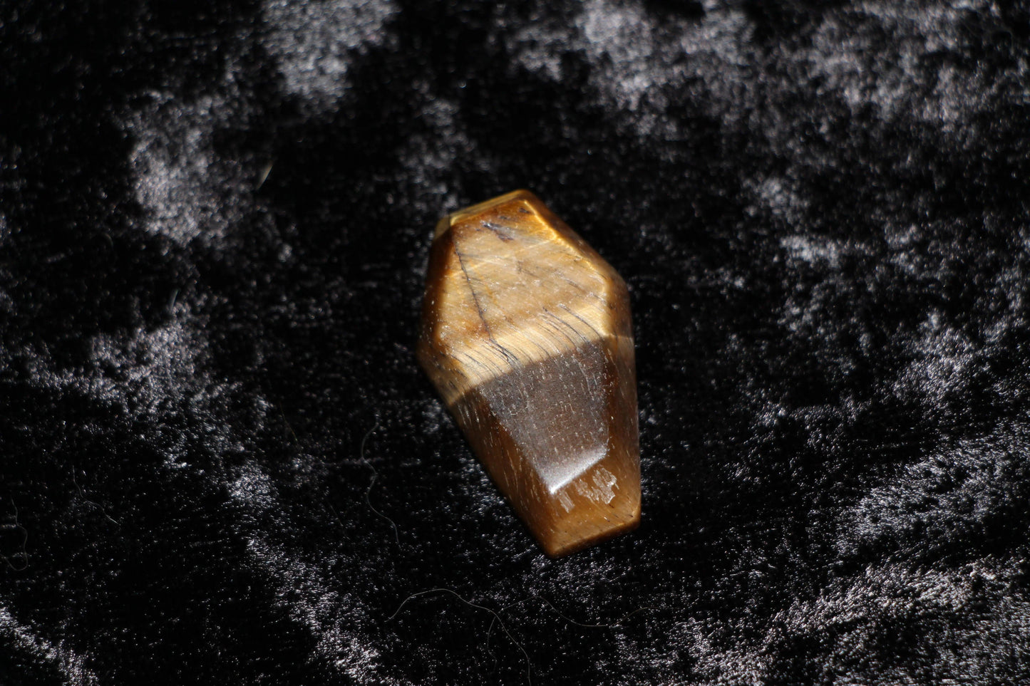 Polished tiger's eye crystal coffin on black velvet, ritual tool for modern witch