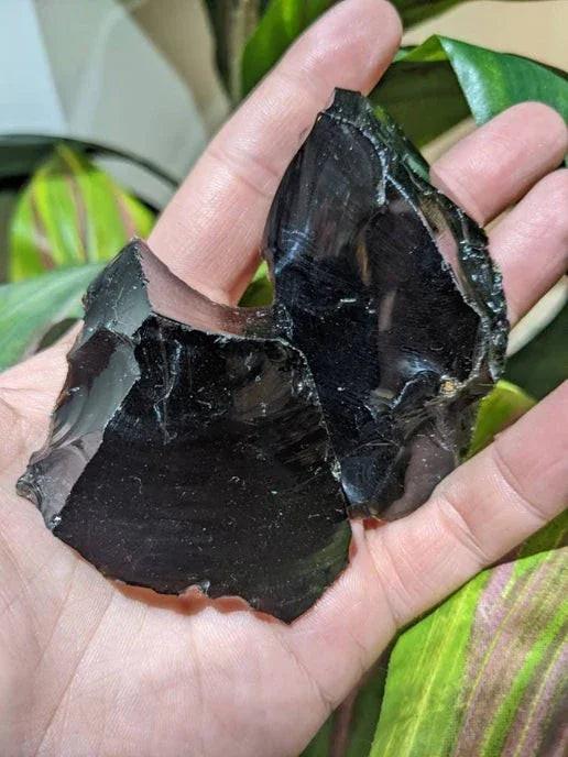Hand holding large raw black obsidian crystals, ideal for witchcraft rituals and intentions