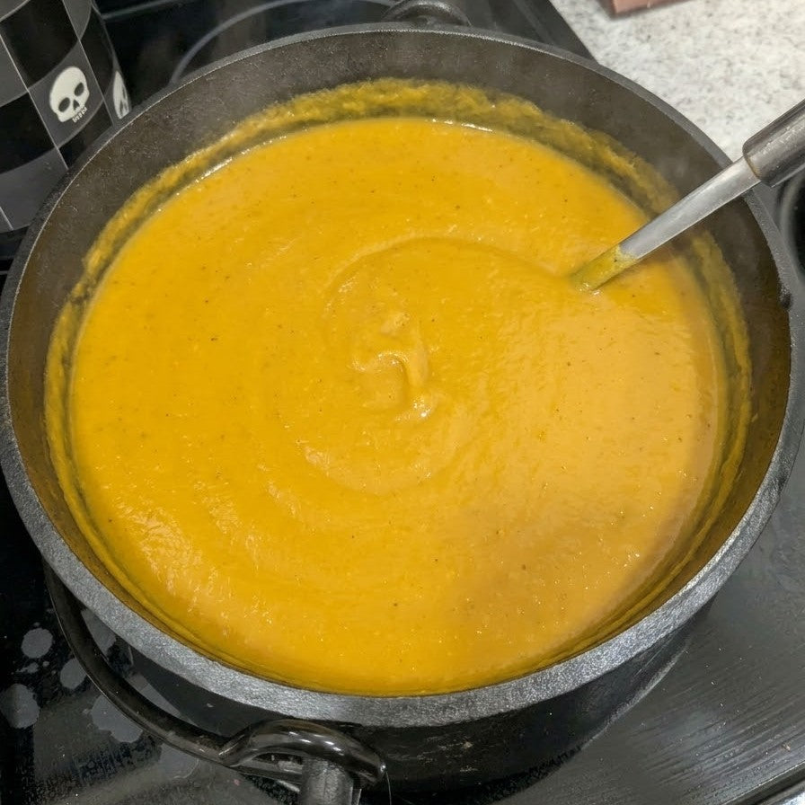Creamy golden pumpkin soup in a saucepan on the stovetop, with a ladle resting inside.