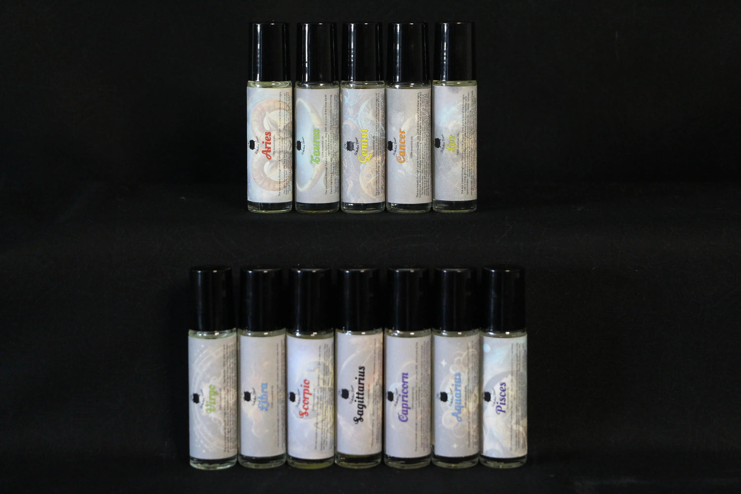 Zodiac essential oil roller bottles set against a black background, each labeled by astrological sign