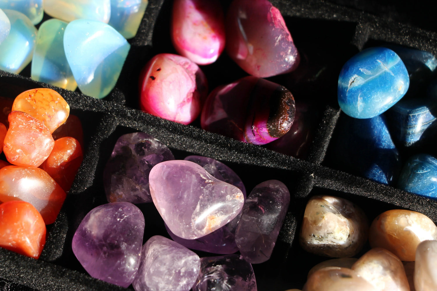 Assorted polished crystals and gemstones in a black display tray, colorful and vibrant