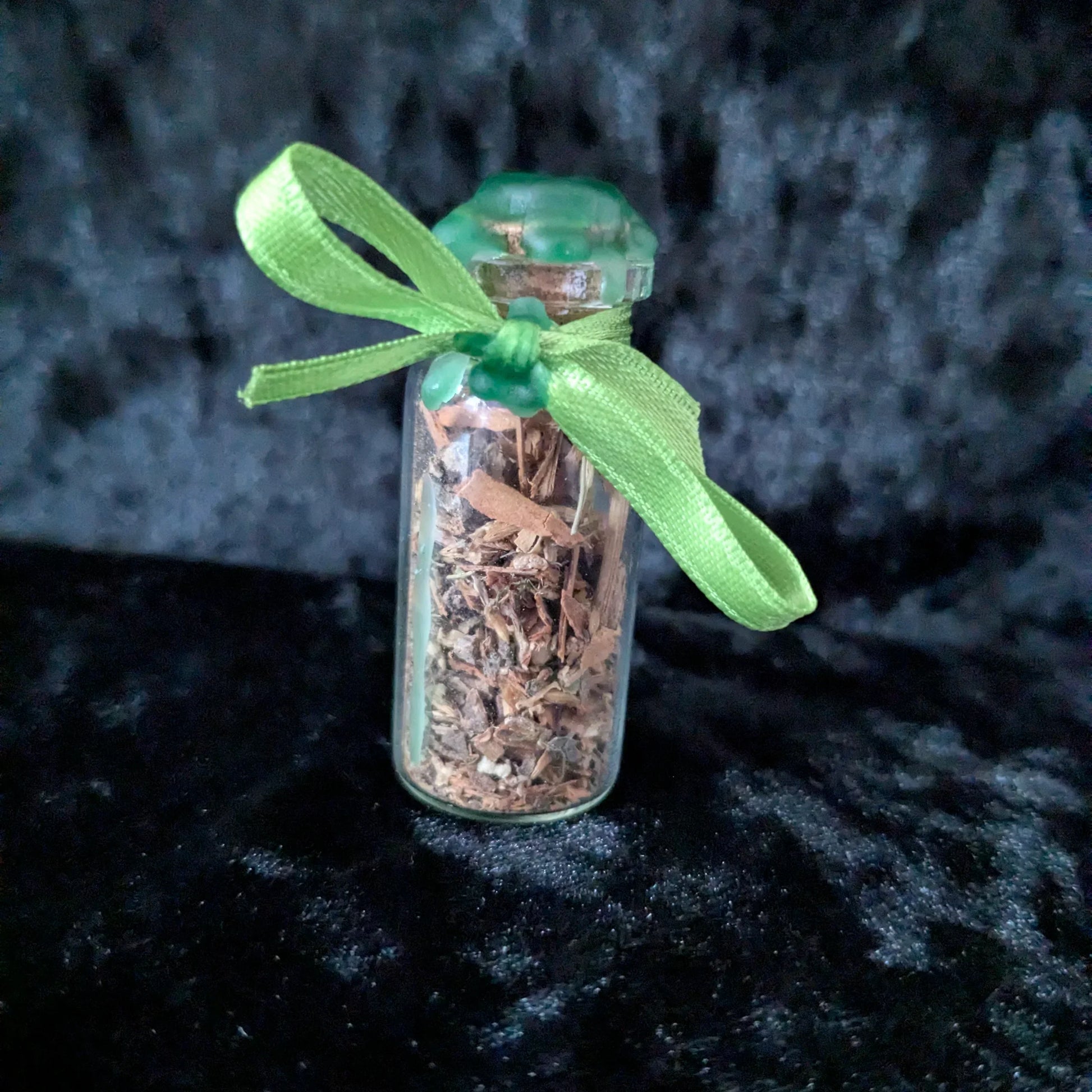 Small glass bottle filled with dried herbs sealed with wax and tied with a green ribbon on dark background
