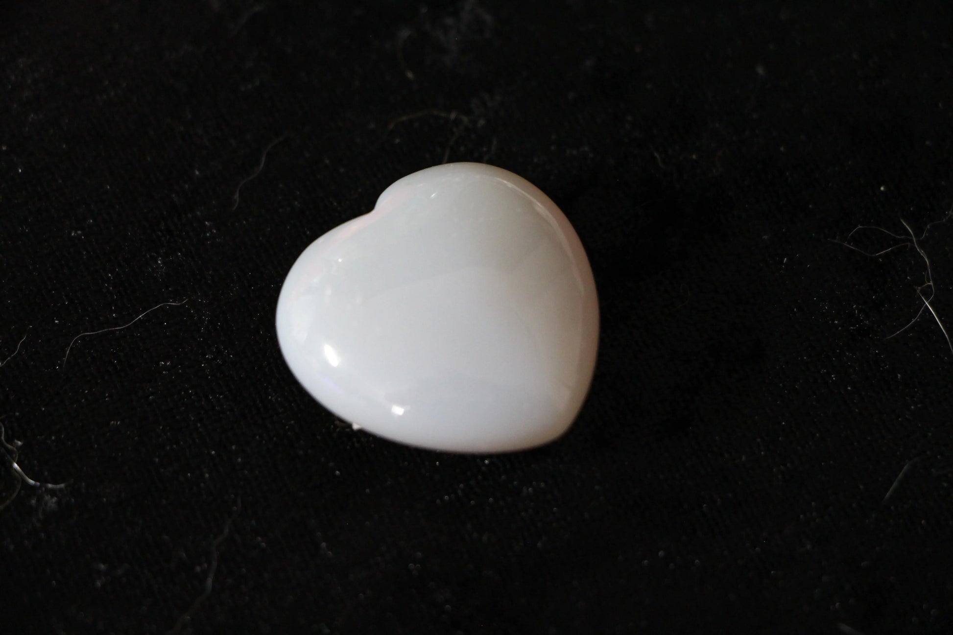 White heart-shaped agate crystal on black fabric, modern witch ritual tool
