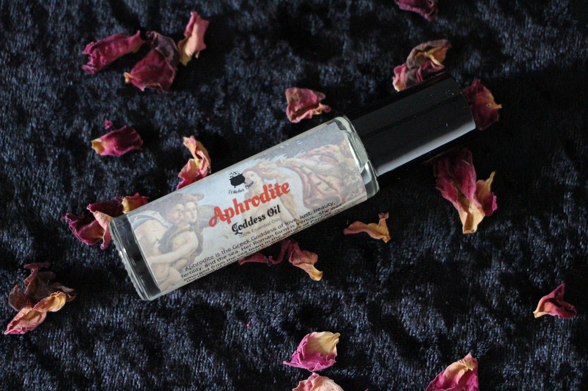 Aphrodite goddess oil roller bottle with dried rose petals on black fabric