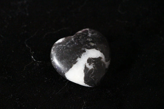 Heart-shaped Black Zebra Jasper crystal stone on a black background, modern witch ritual tool