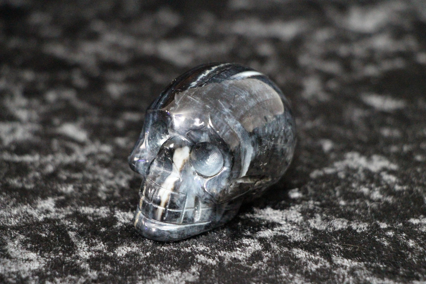 polished black banded agate crystal skull on textured dark background