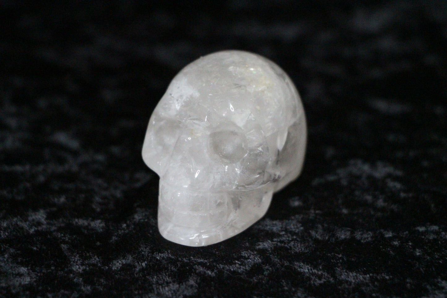 Clear quartz crystal skull carving on black velvet surface