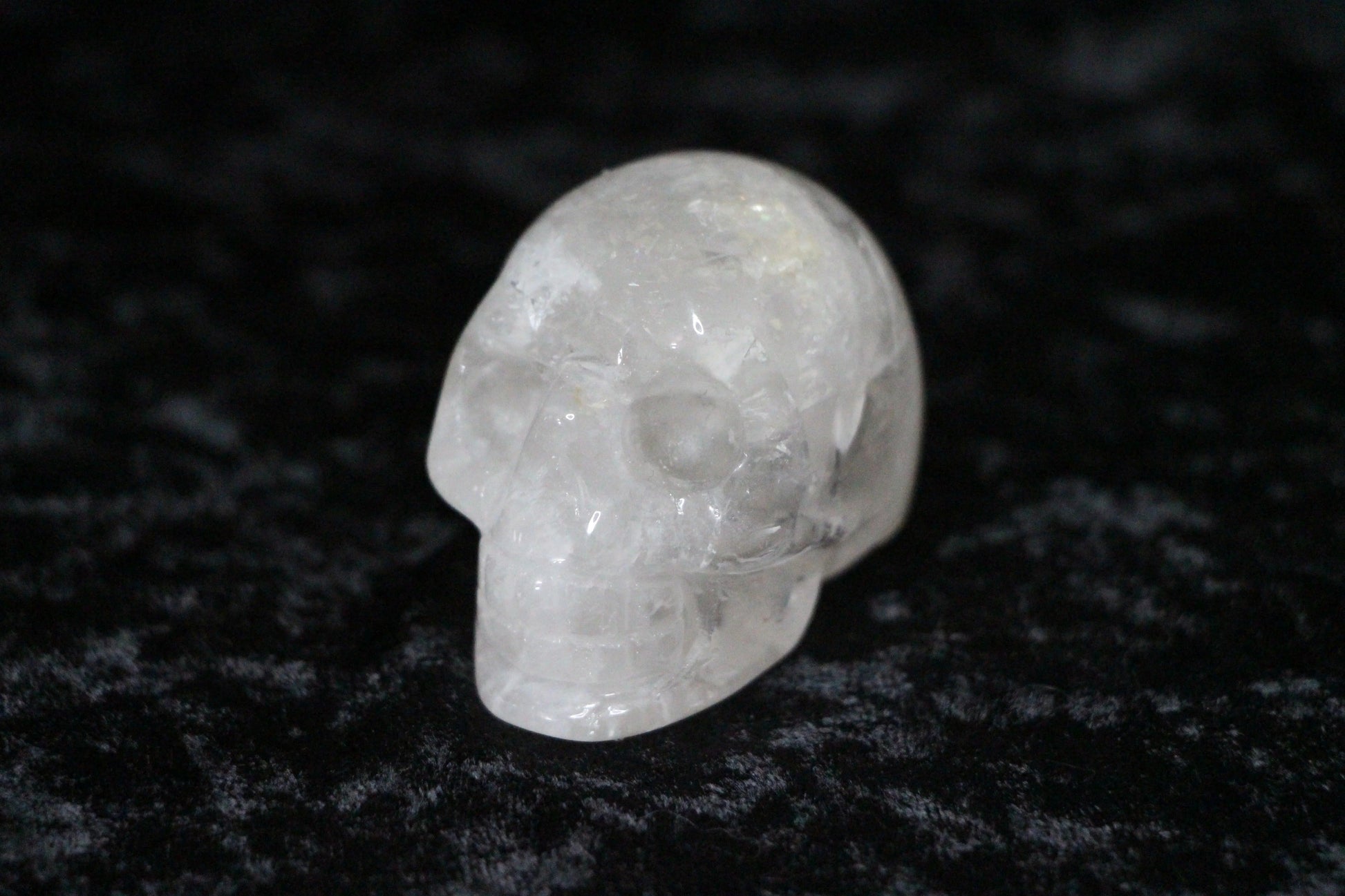 Clear quartz crystal skull carving on black velvet surface