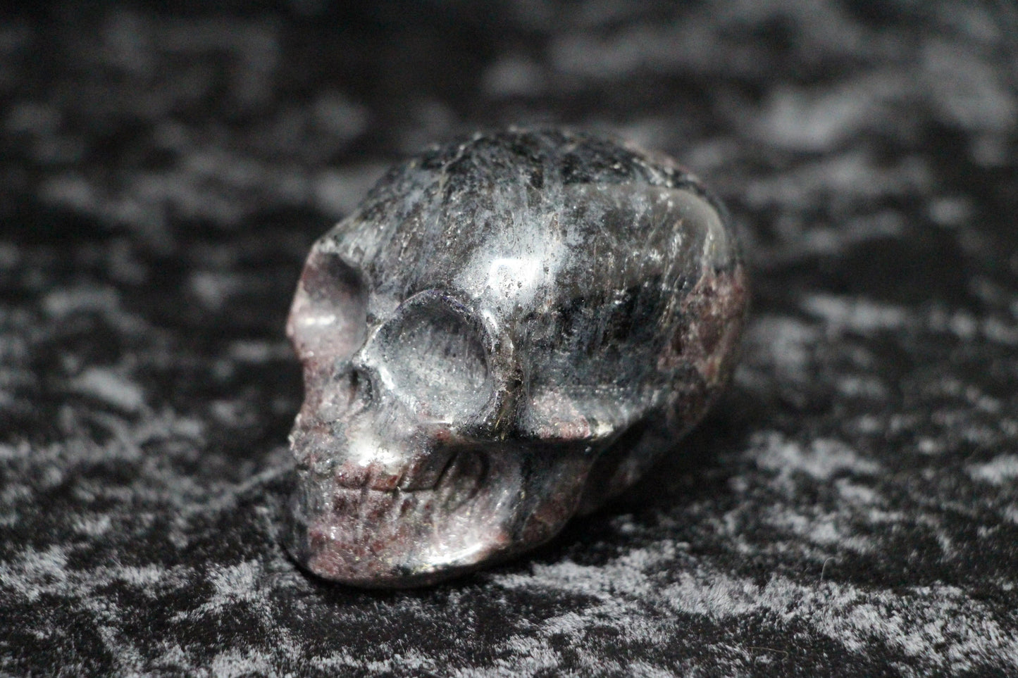 Polished garnet crystal skull carving on a textured black surface