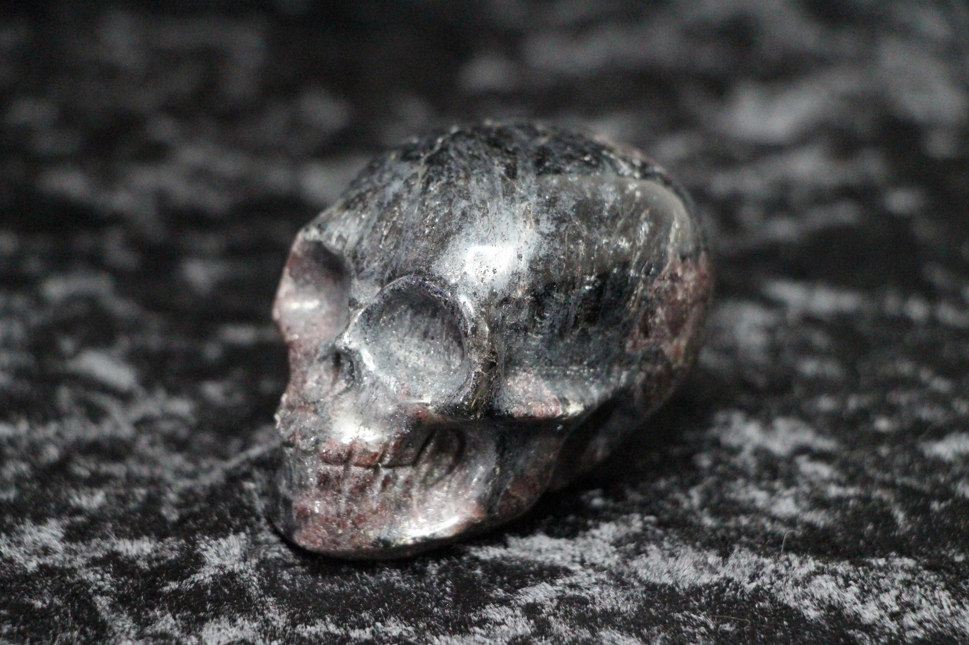 Polished garnet crystal skull carving on a textured black surface