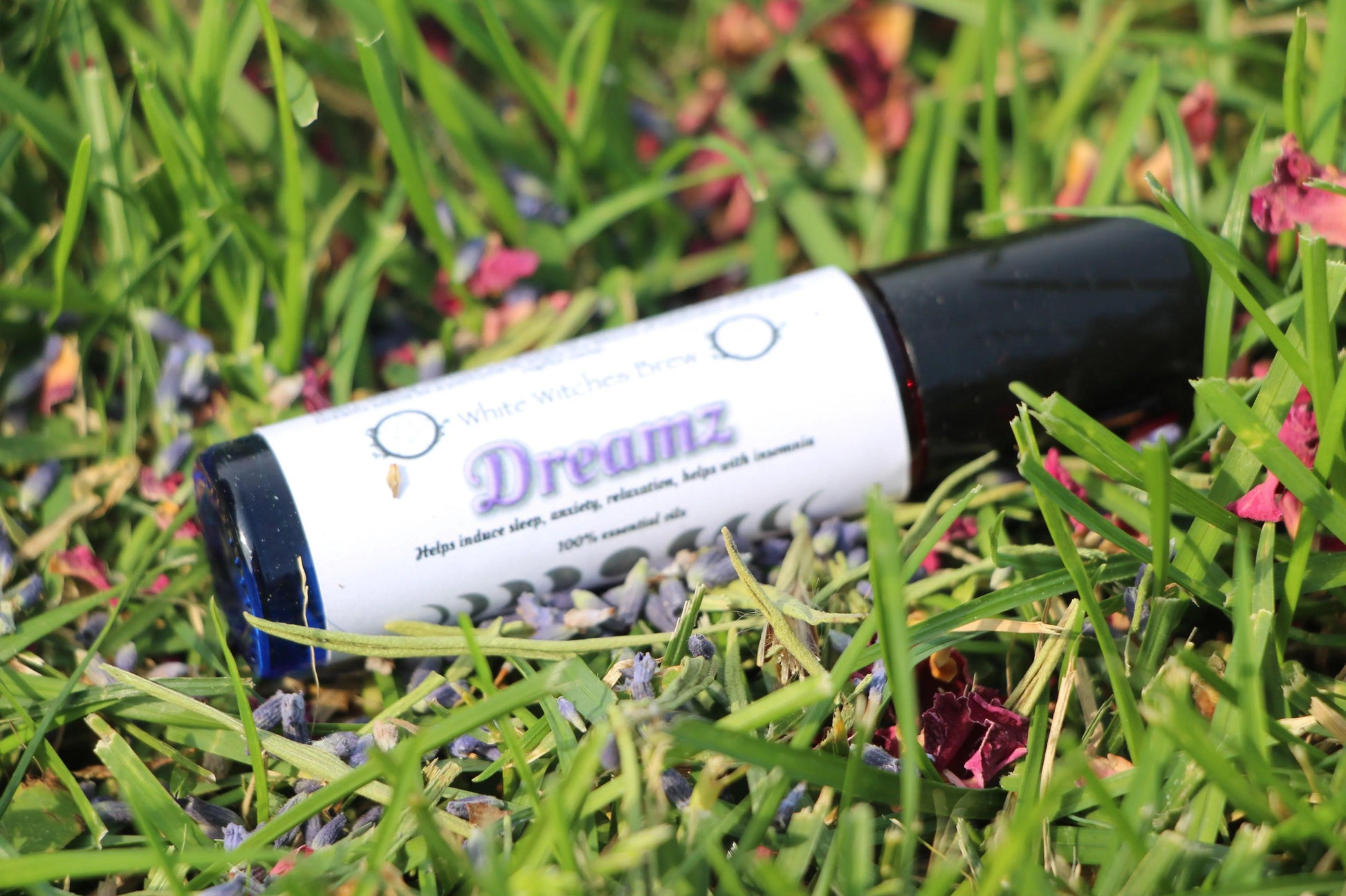 Dreamz essential oil roller on grass with flower petals, hand-crafted aromatherapy for sleep
