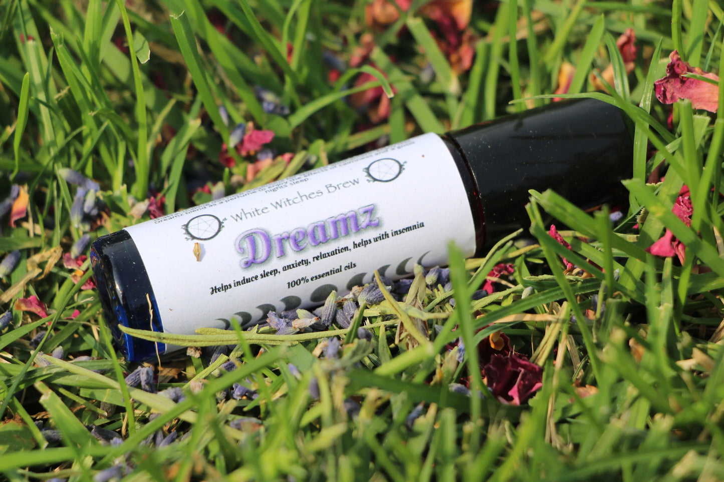 White Witches Brew Dreamz essential oil roll-on in grass with dried flowers, natural setting