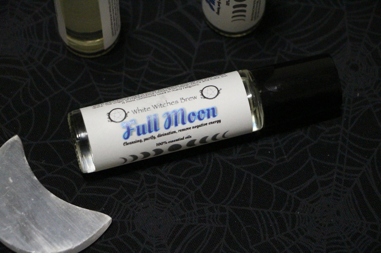 White Witches Brew Full Moon essential oil roller on spiderweb fabric with a crescent-shaped crystal
