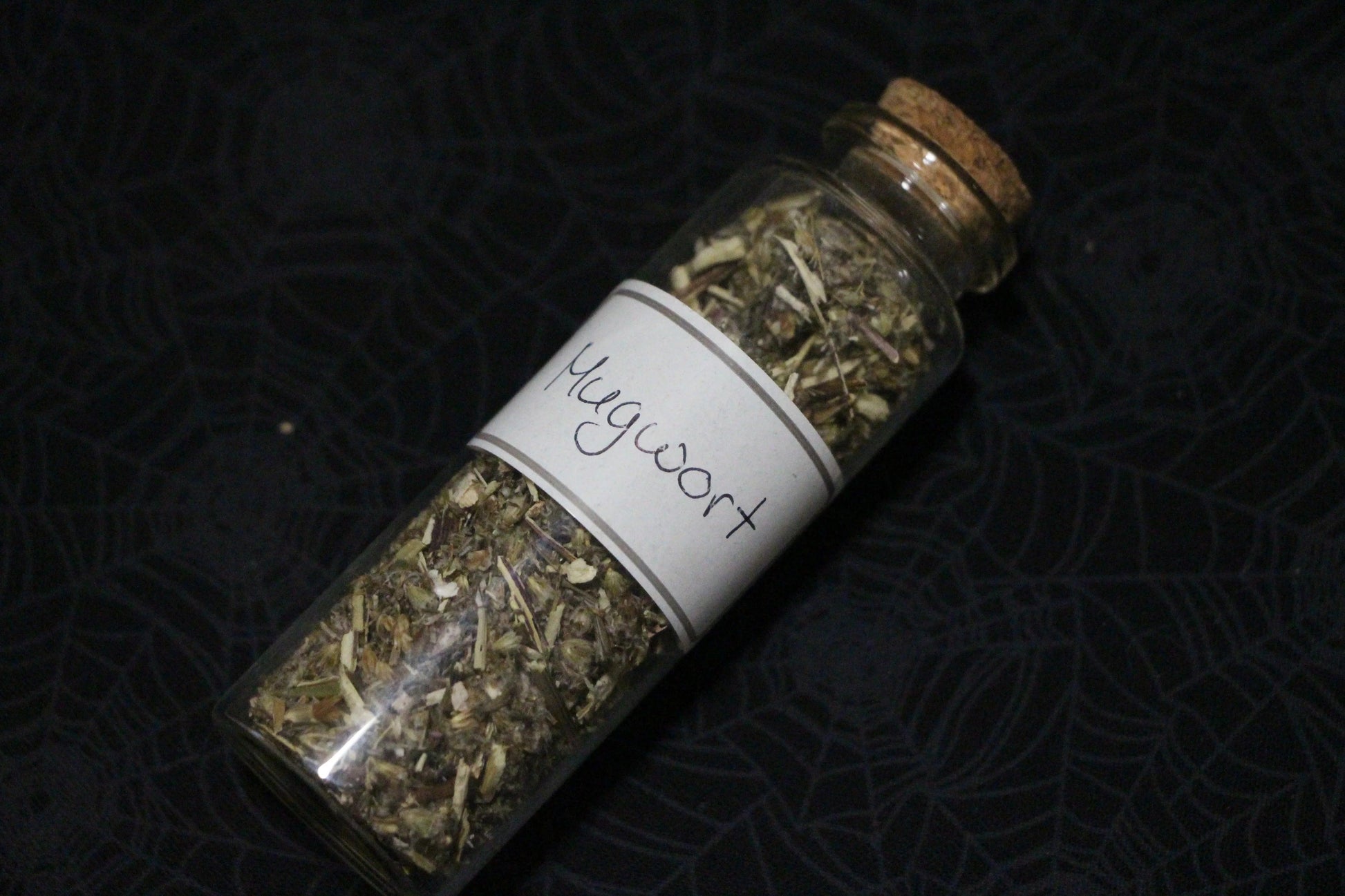 Glass jar of dried mugwort labeled for witchcraft rituals on black spiderweb cloth