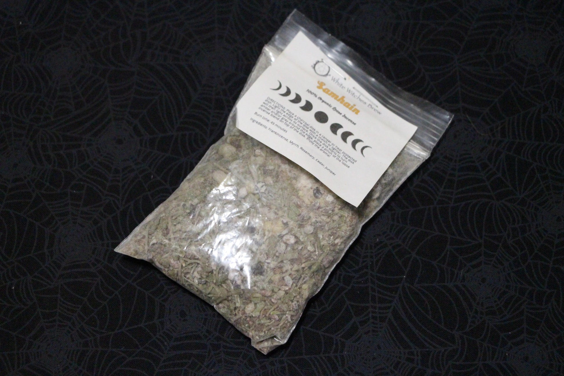 Herbal incense blend in clear pouch with moon phase label on black spiderweb background, Witches' Brew