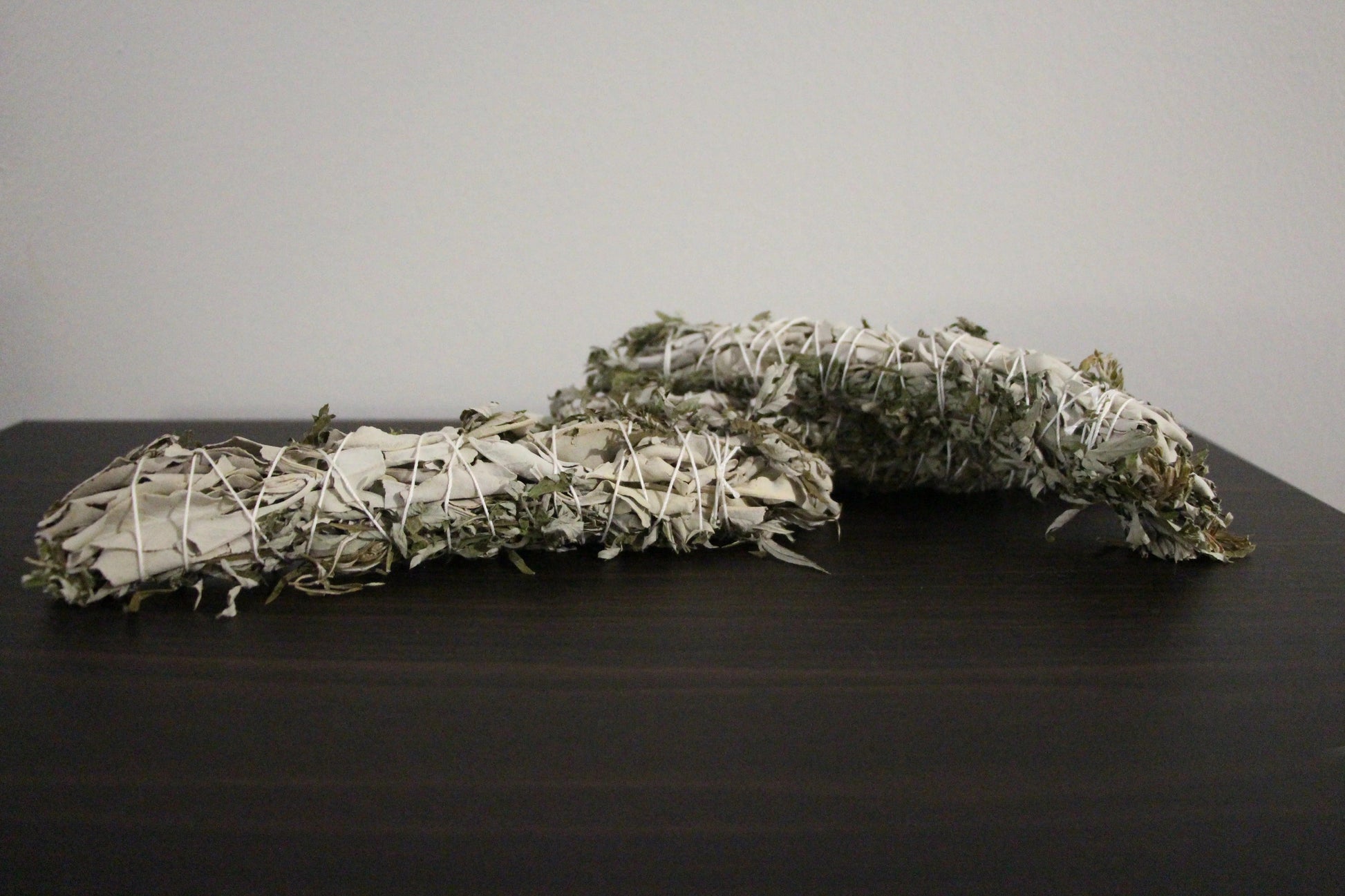 Hand-crafted sage bundles wrapped in white string on a dark wooden surface