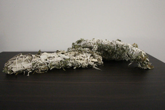 Hand-crafted sage bundles wrapped in white string on a dark wooden surface