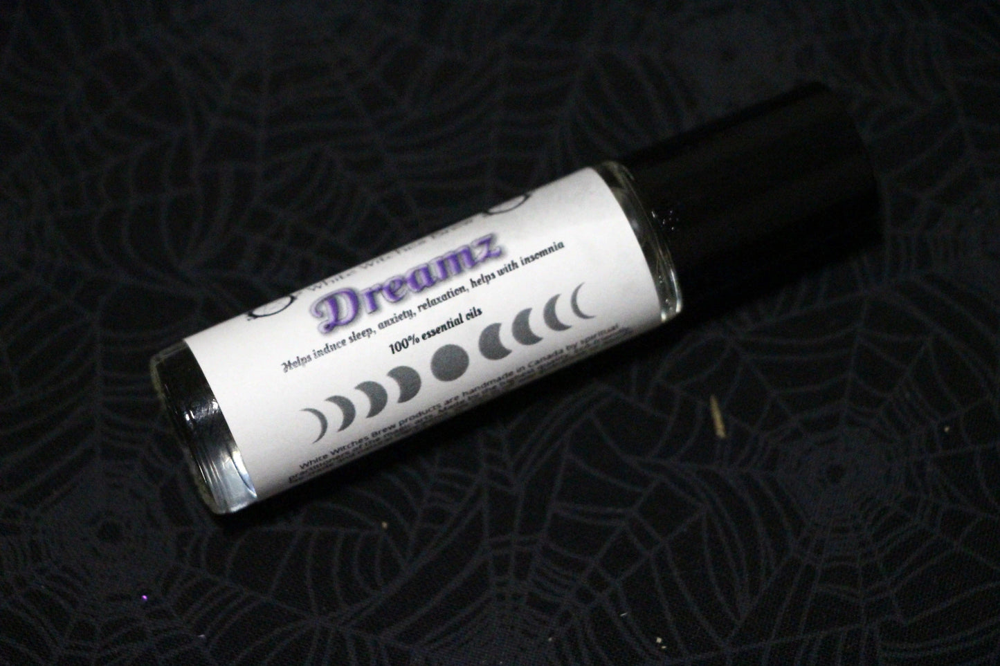 Dreamz essential oil roll-on bottle with moon phases, on black spiderweb fabric