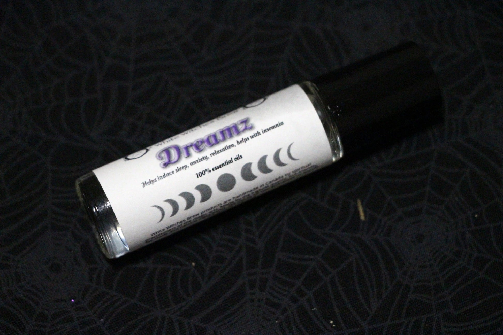 Dreamz essential oil roll-on bottle with moon phases, on black spiderweb fabric