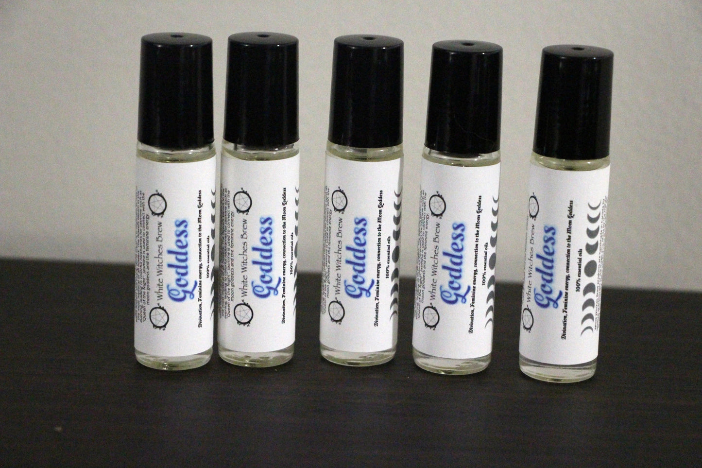 Five roll-on bottles of Goddess essential oil by White Witches Brew with black caps on dark surface
