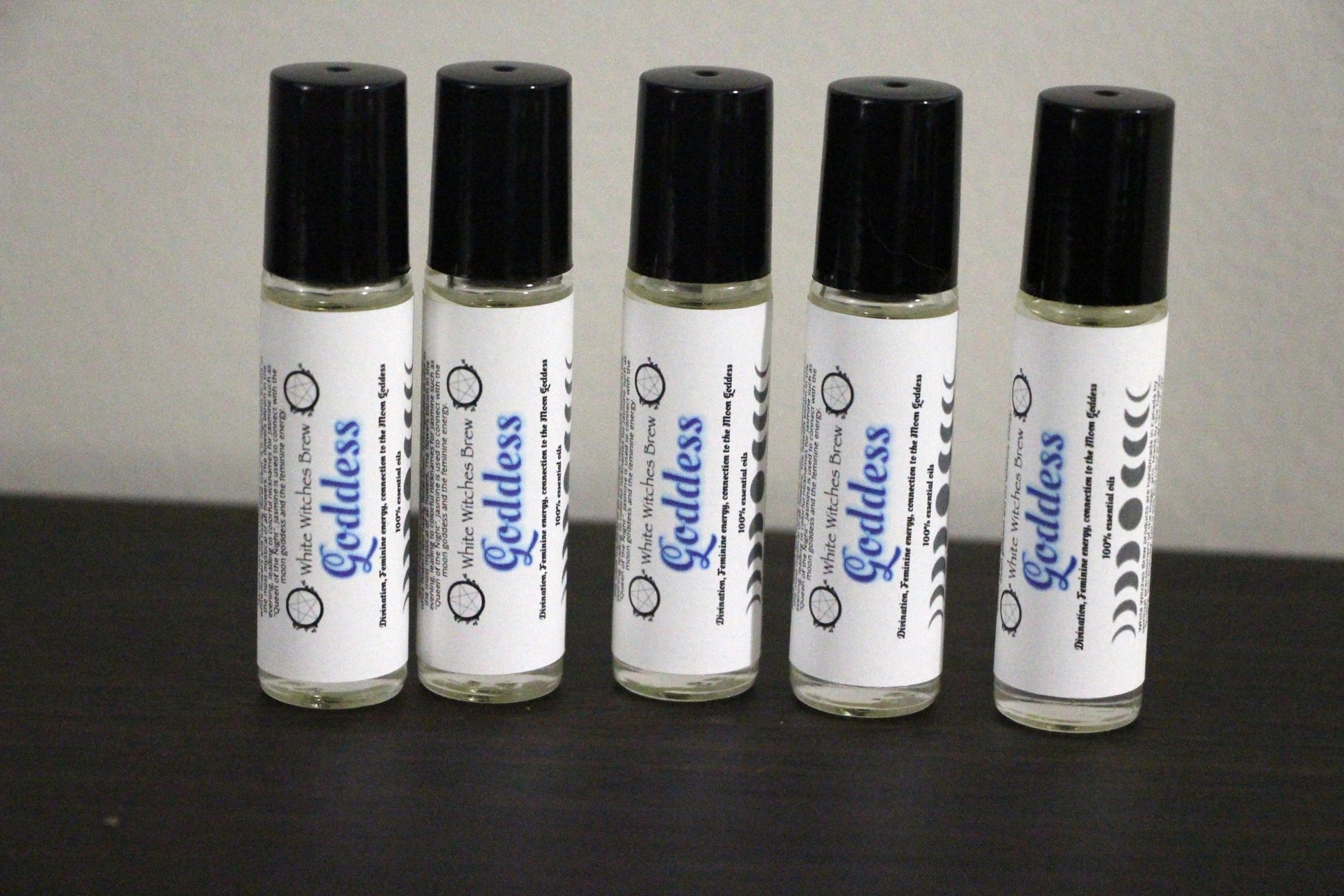 Five roll-on bottles of Goddess essential oil by White Witches Brew with black caps on dark surface