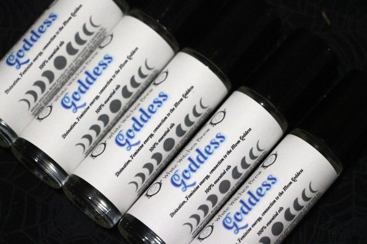Roll-on bottles labeled Goddess essential oils with moon phases and spiritual symbols on black background
