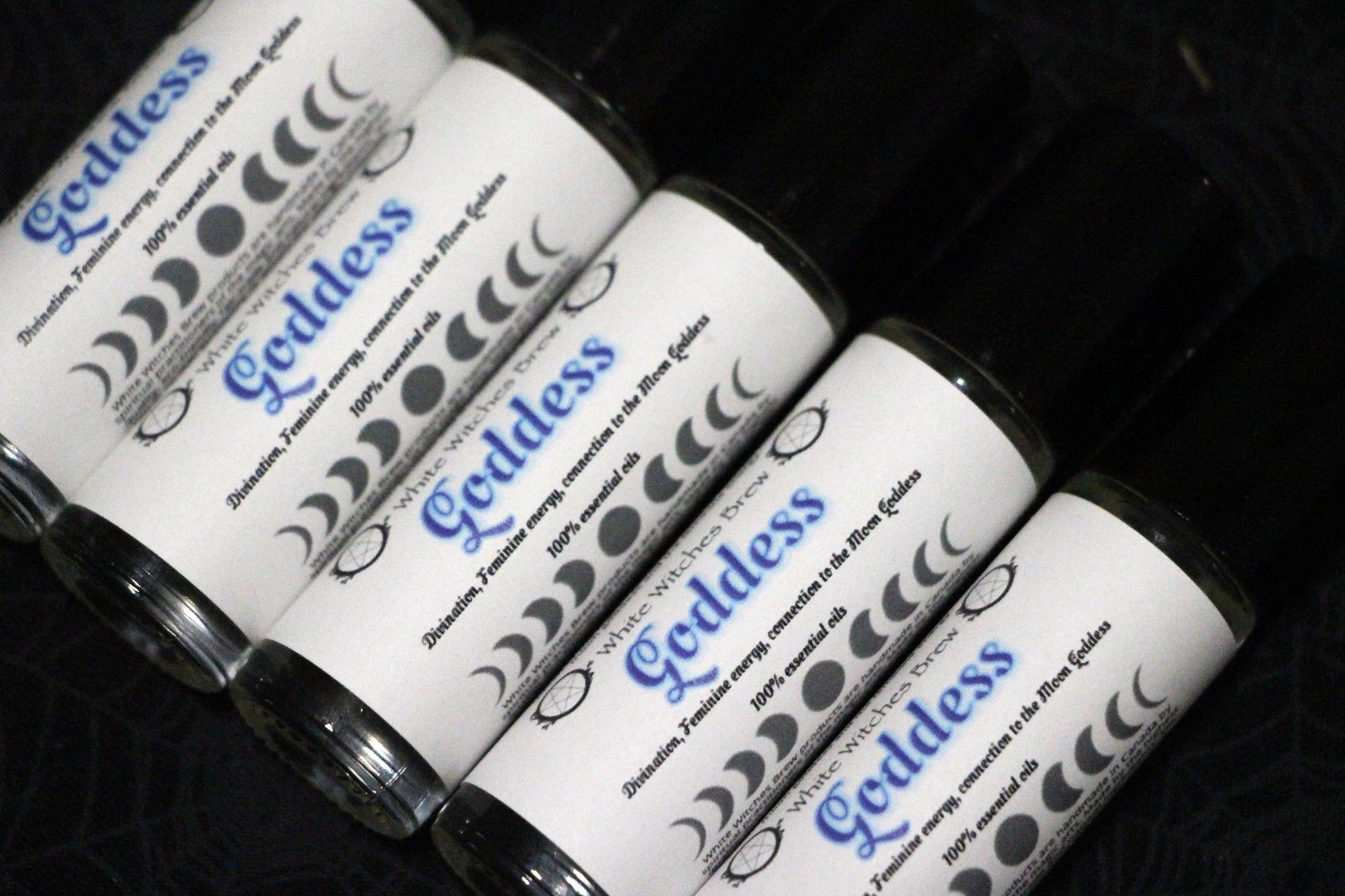 Roll-on bottles labeled Goddess essential oils with moon phases and spiritual symbols on black background