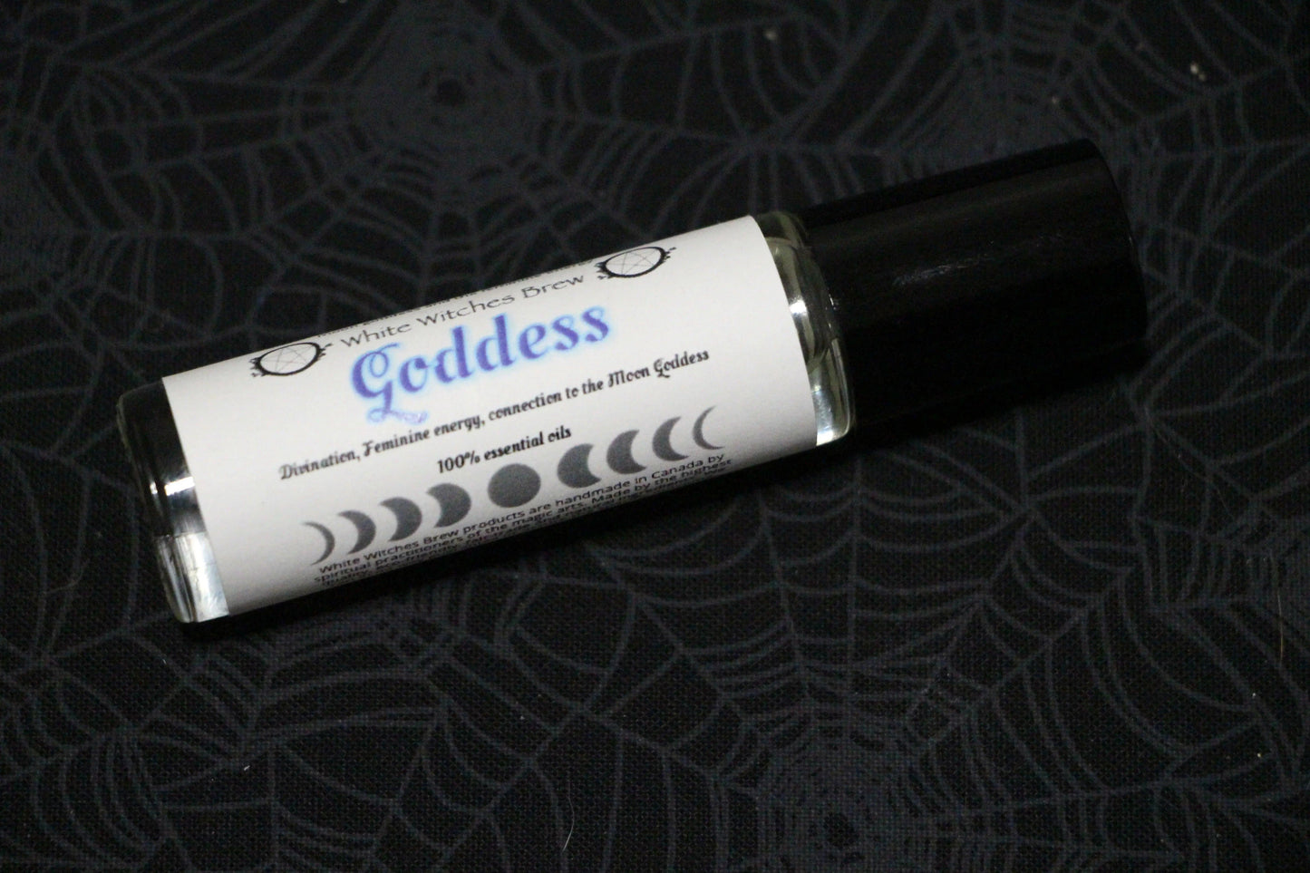 White Witches Brew Goddess essential oil roll-on on black spider web patterned fabric