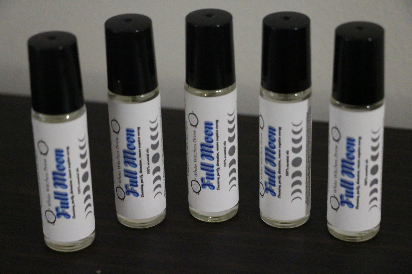 Five Full Moon essential oil roll-on bottles with black caps on a dark surface
