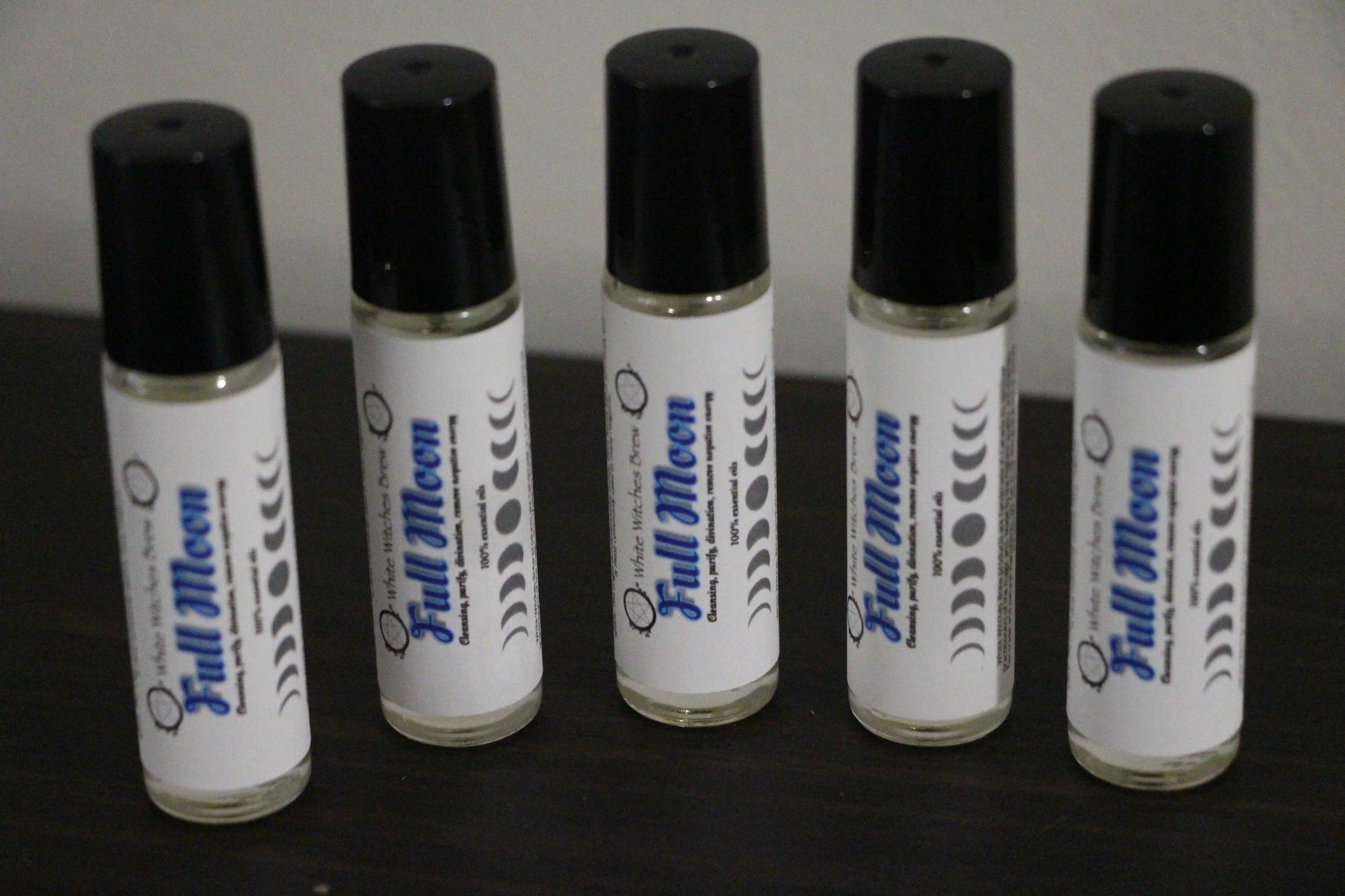 Five Full Moon essential oil roll-on bottles with black caps on a dark surface