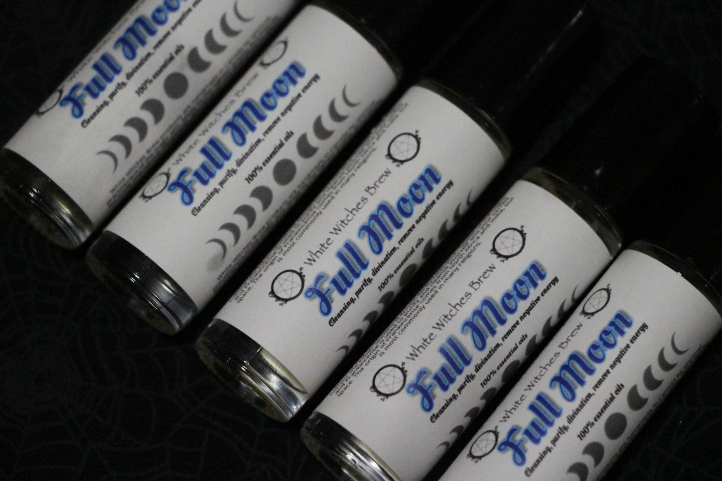 Row of Full Moon essential oil roll-on bottles with moon phase labels on dark surface