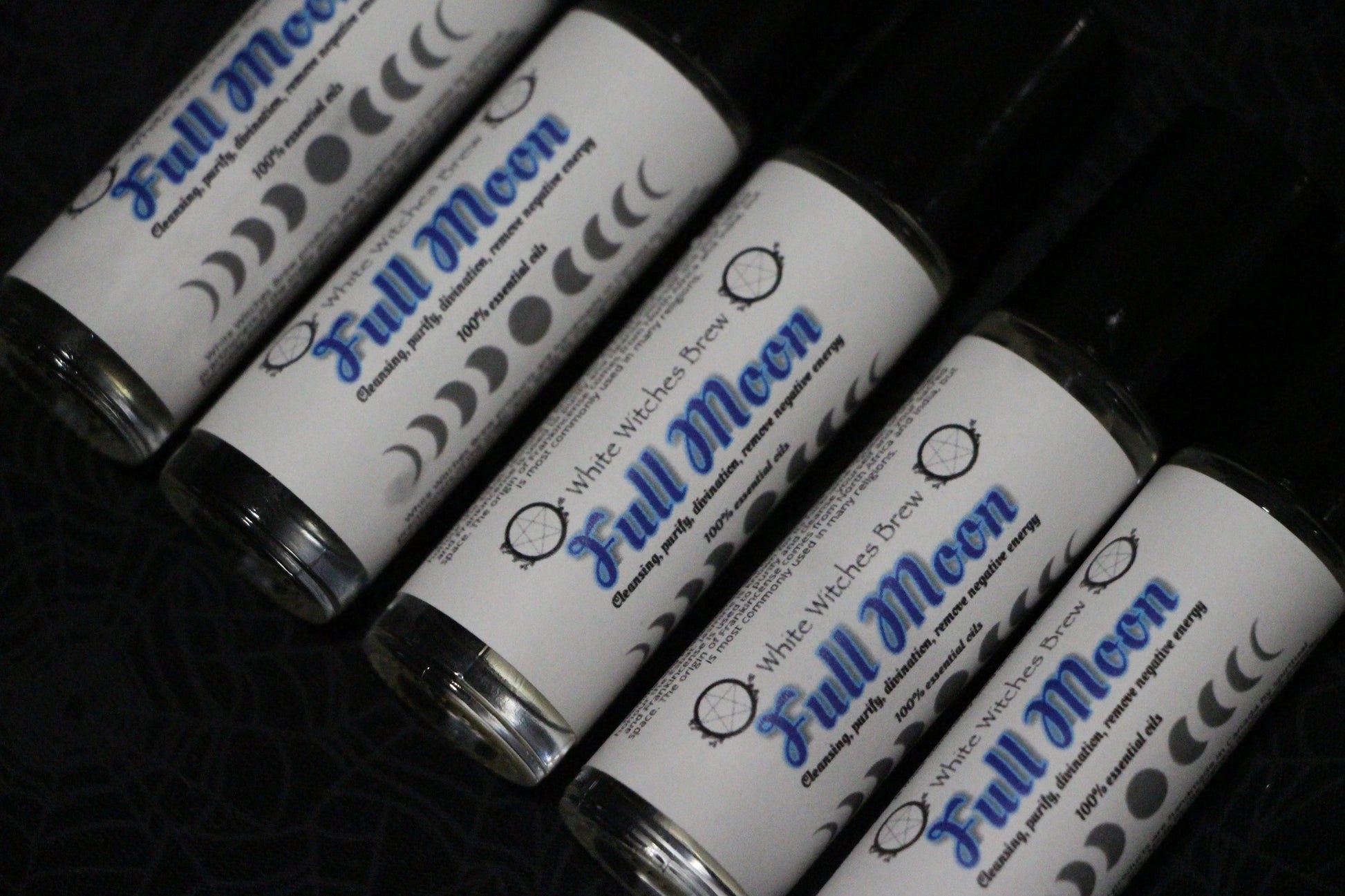 Row of Full Moon essential oil roll-on bottles with moon phase labels on dark surface