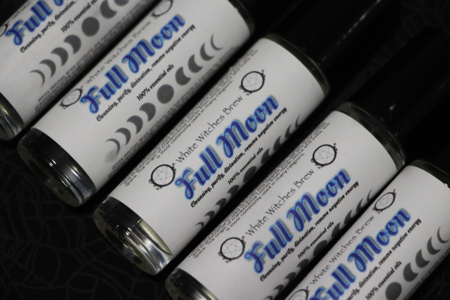 Roll-on bottles labeled Full Moon essential oils with moon phase symbols on black fabric