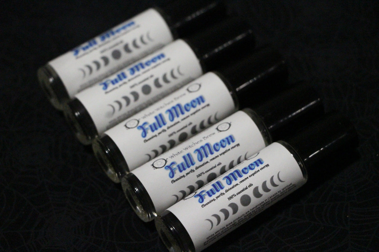 Five Full Moon essential oil roll-on bottles arranged diagonally on a dark patterned surface