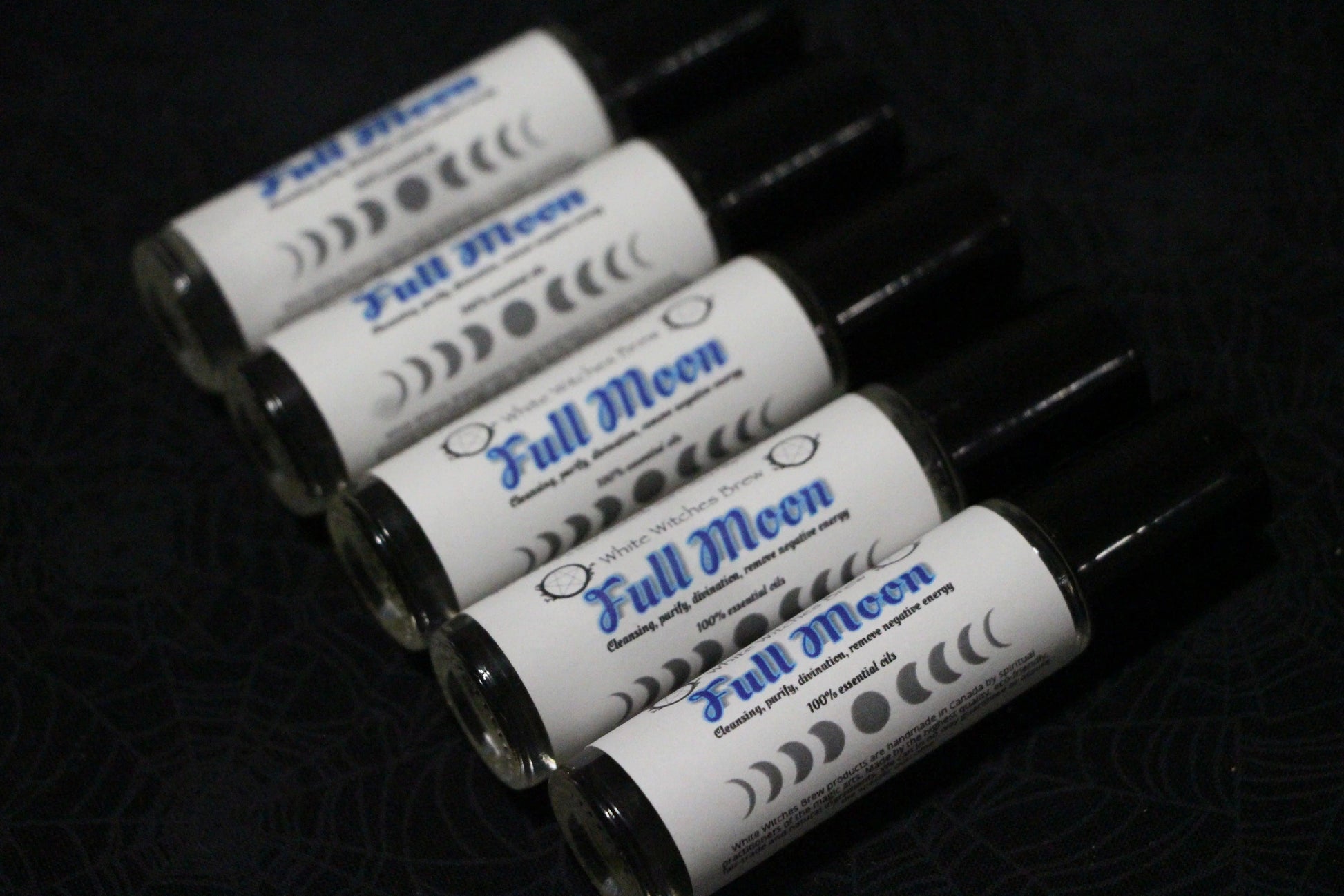 Five Full Moon essential oil roll-on bottles arranged diagonally on a dark patterned surface