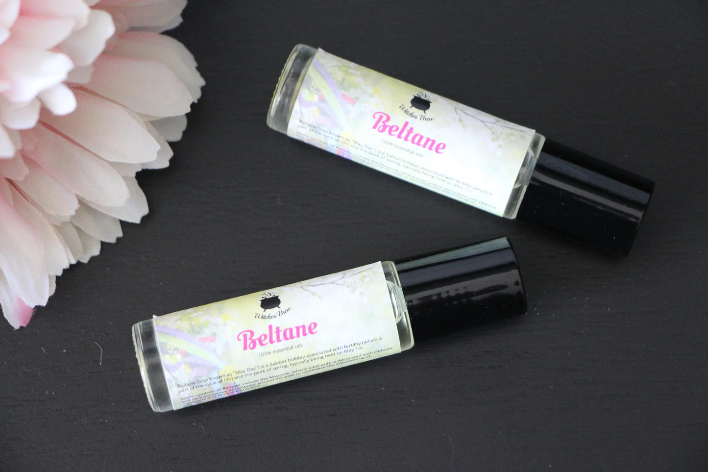 Beltane essential oil roller bottles on black surface beside pink flower