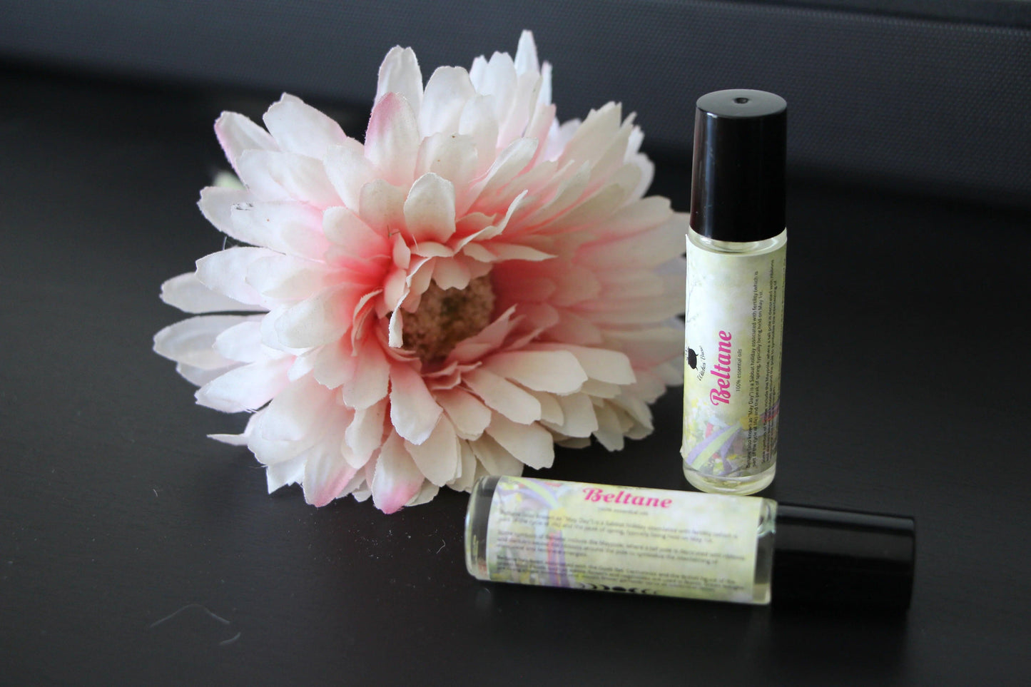 Beltane essential oil roller bottles with pink and white flower on black background