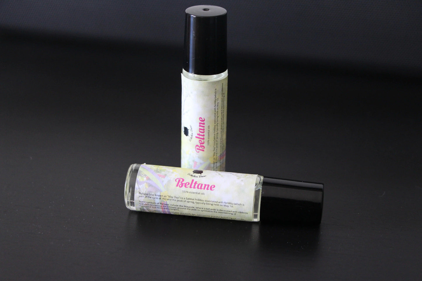 Beltane essential oil rollers with black caps on a black surface, hand-crafted ritual tool