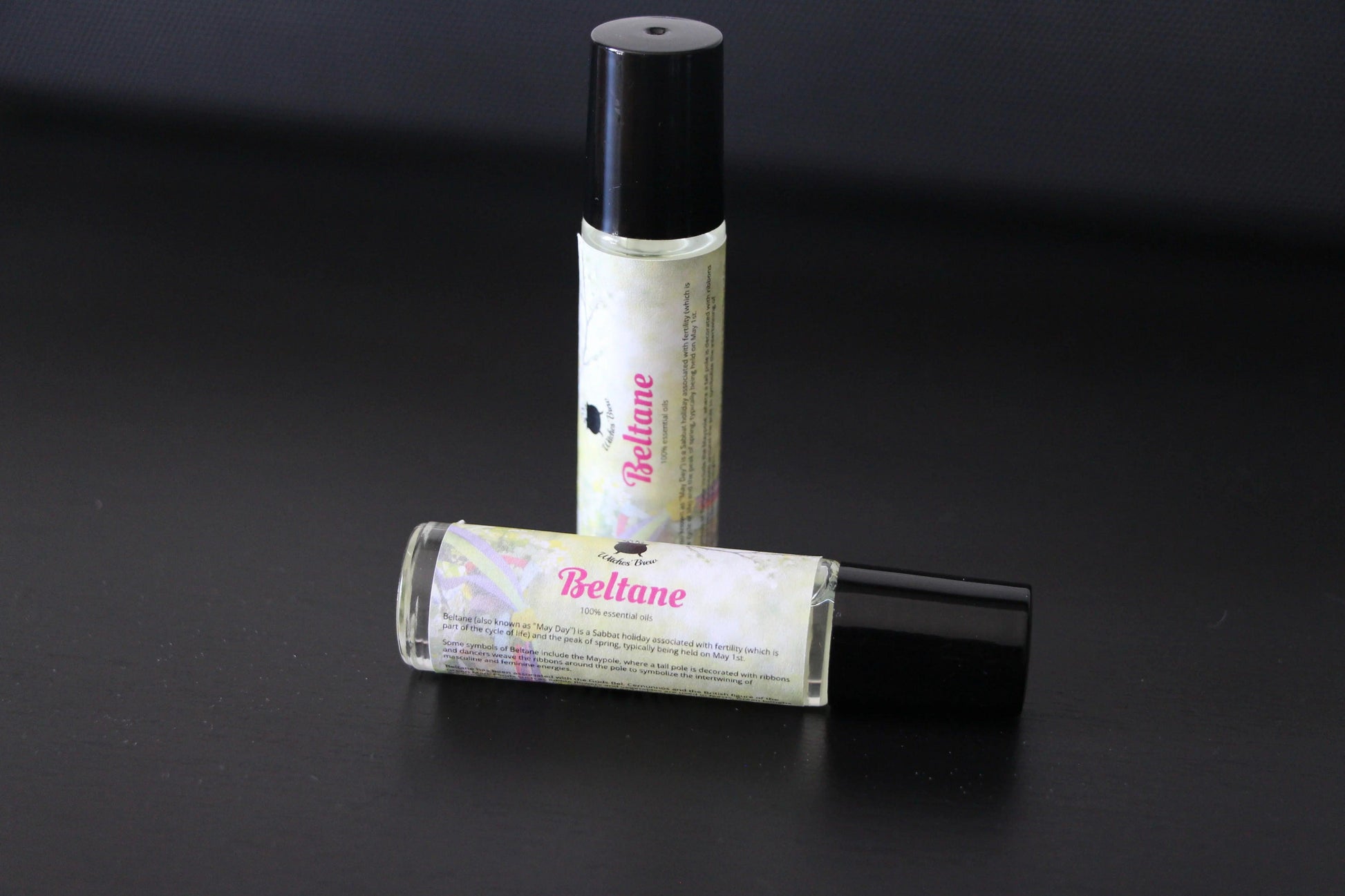 Beltane essential oil rollers with black caps on a black surface, hand-crafted ritual tool