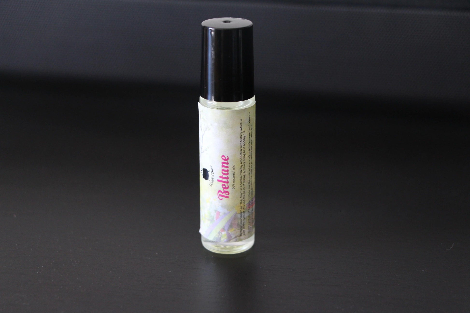 Beltane essential oil roller bottle with black cap on a dark surface, ritual aromatherapy
